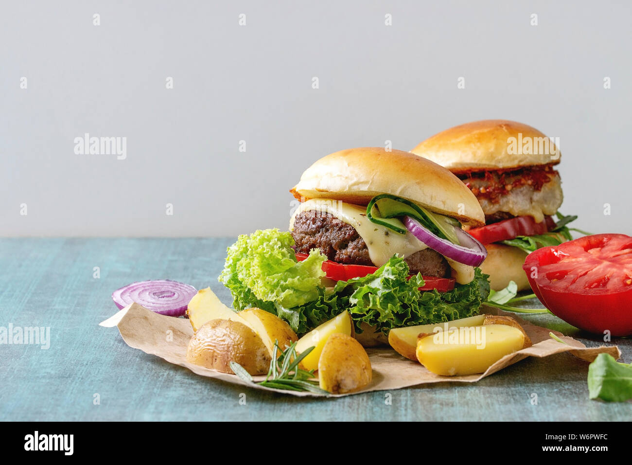 Zwei selbstgemachte Fast Food Burger classic Hamburger oder Cheeseburger mit Rindfleisch, Salat, Käse und Tomaten serviert auf Papier mit gebackenen Land Kartoffeln auf Bl Stockfoto