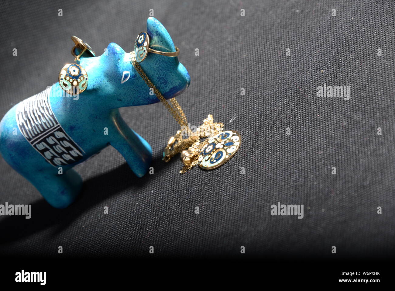 Schmuck auf die kleine blaue rhino Statue halten Sie den Schmuck Halter blau Halskette Gold Ringe Blau und Gold Ringe mit grauem Hintergrund hübsches Tier Stockfoto