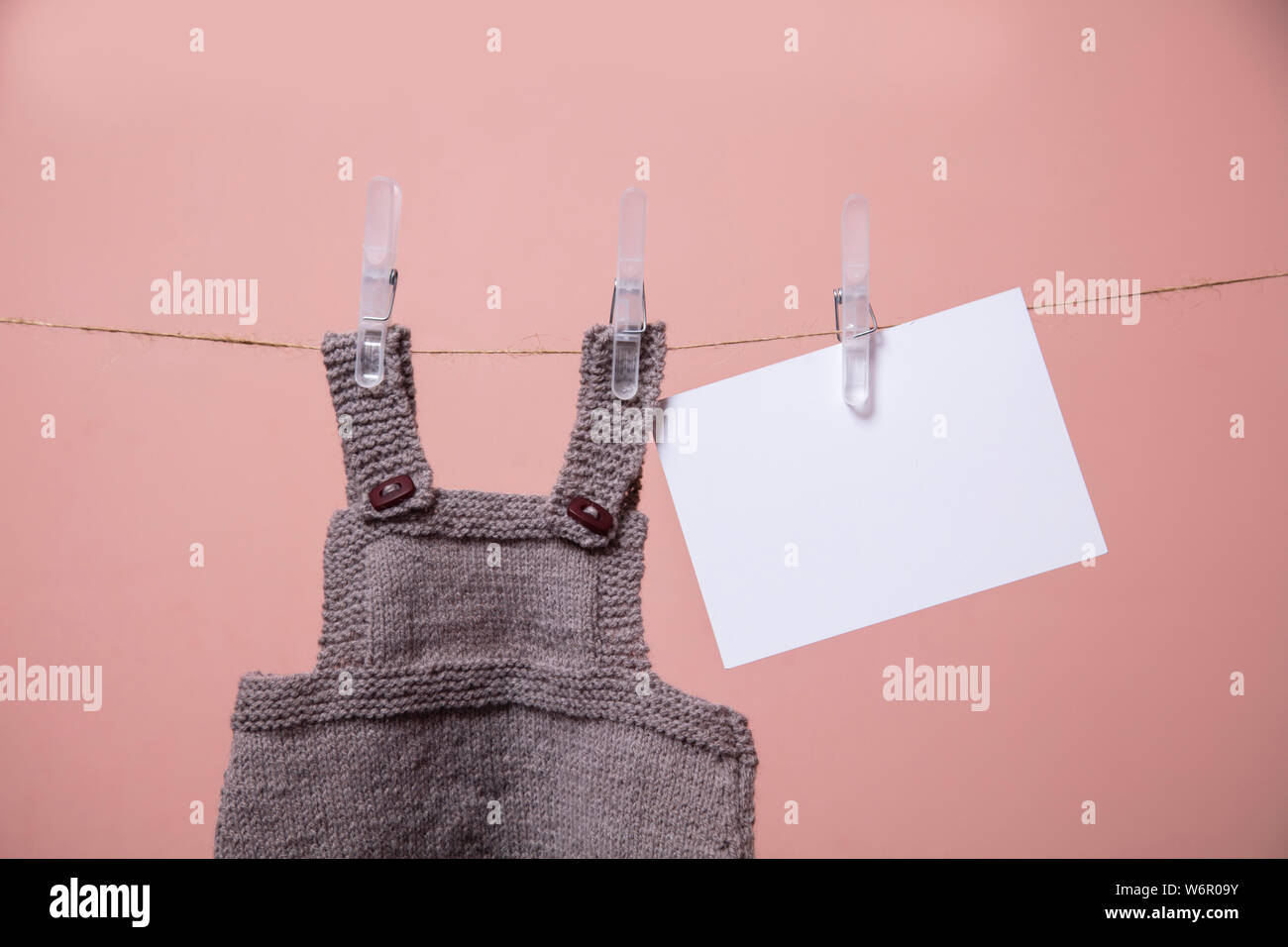 Gestrickte Baby Kleidung und eine leere Karte hängen an einer Wäscheleine Stockfoto