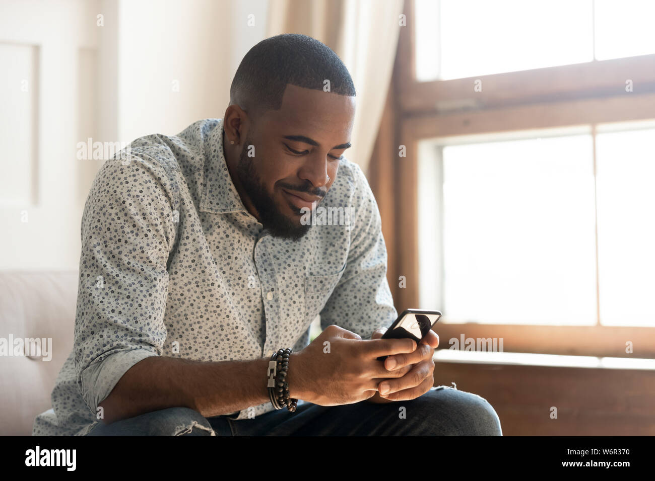 Junge afrikanische amerikanische Mann mit Smartphone App sitzen auf dem Sofa Stockfoto