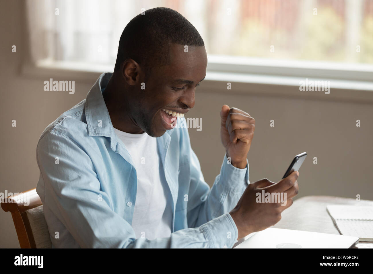 Afrikanischer mann Blick auf Smartphone fühlt sich gut Nachricht begeistert empfangen Stockfoto