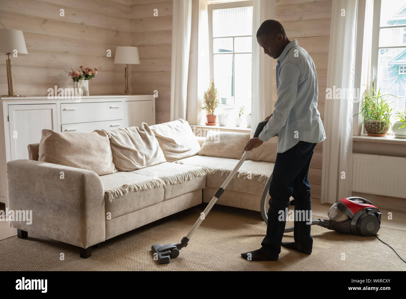 Afrikanische Kerl mit Staubsauger reinigen Teppich im Wohnzimmer Stockfoto