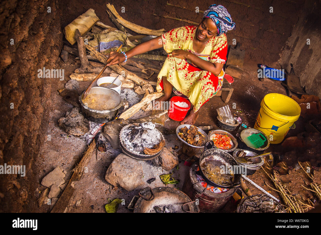 Sansibar, Tansania, März 29, 2018 Eine afrikanische Frau in Nationale Kleidung Köche eine einfache nationalen Mahlzeit in einem alten, schmutzigen Teller in einer Hütte auf einem tönernen Boden Stockfoto