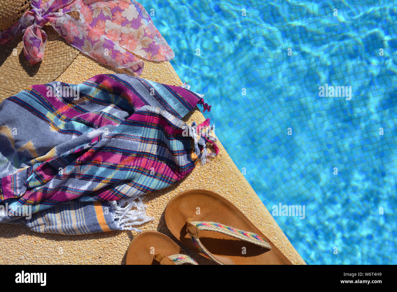 Sommer flatlay, Stroh Hut mit Schal, Strand wickeln und Sandalen an der Seite eines blau gefliesten Pool. mit Platz kopieren Stockfoto