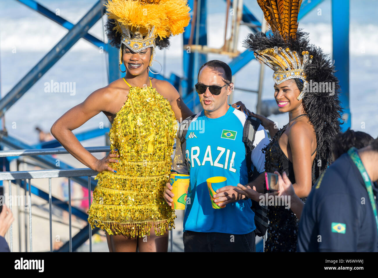Mann mit zwei Frauen im Karneval Outfit während der Olympischen Spiele 2016 auf einen temporären Stand am Strand von Copacabana mit dem Ozean im Hinterg Stockfoto