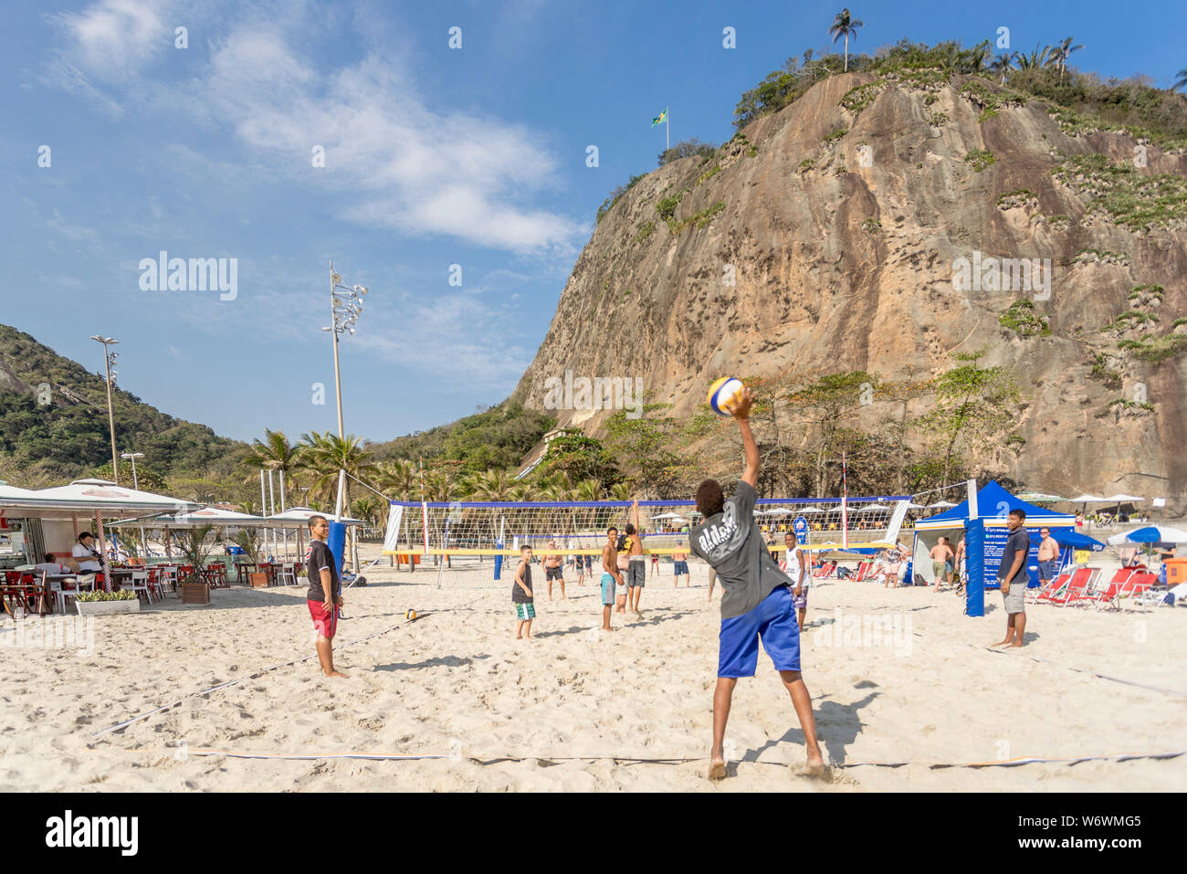 Jugendliche serviert in einer Partie Beachvolleyball am Copacabana Strand an einem sonnigen Tag mit dem Leme Berg im Hintergrund Stockfoto