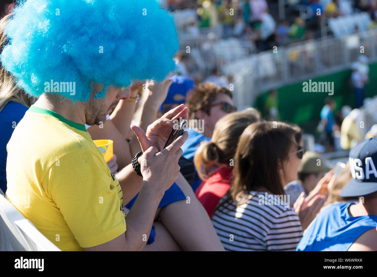 Brasilianischen Anhänger mit blauen Perücke auf, auf sein Handy statt Was ist los im Stadion mit Masse im Hintergrund Stockfoto