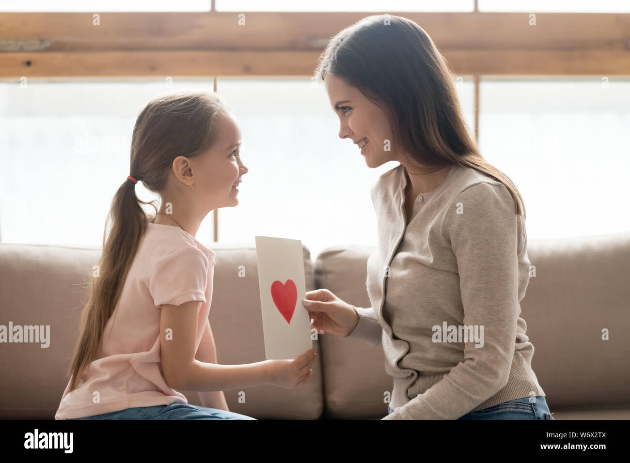 Tochter und Mutter sitzen auf der Couch Holding handgefertigte Postkarte Stockfoto