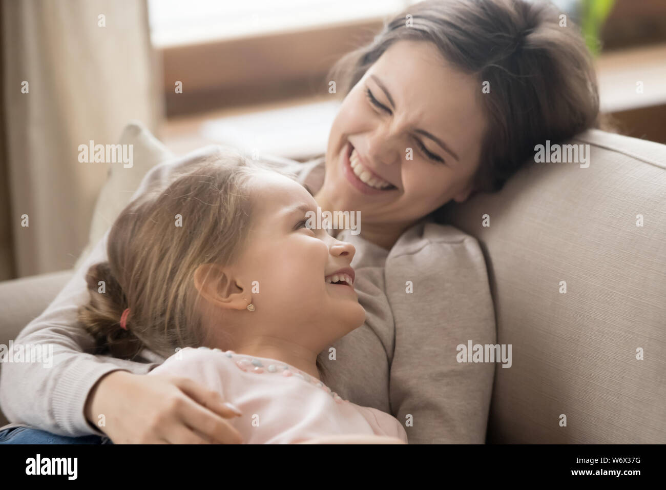 Tochter im Vorschulalter und fröhliche Mutter liegt auf der Couch Witze lachen Stockfoto