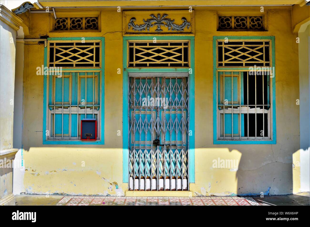 Eingang zu den traditionellen Peranakan shop Haus mit blauen und cremefarbenen antiken Tür und Fenster auf gelbe Wand im historischen Geylang, Singapur Stockfoto