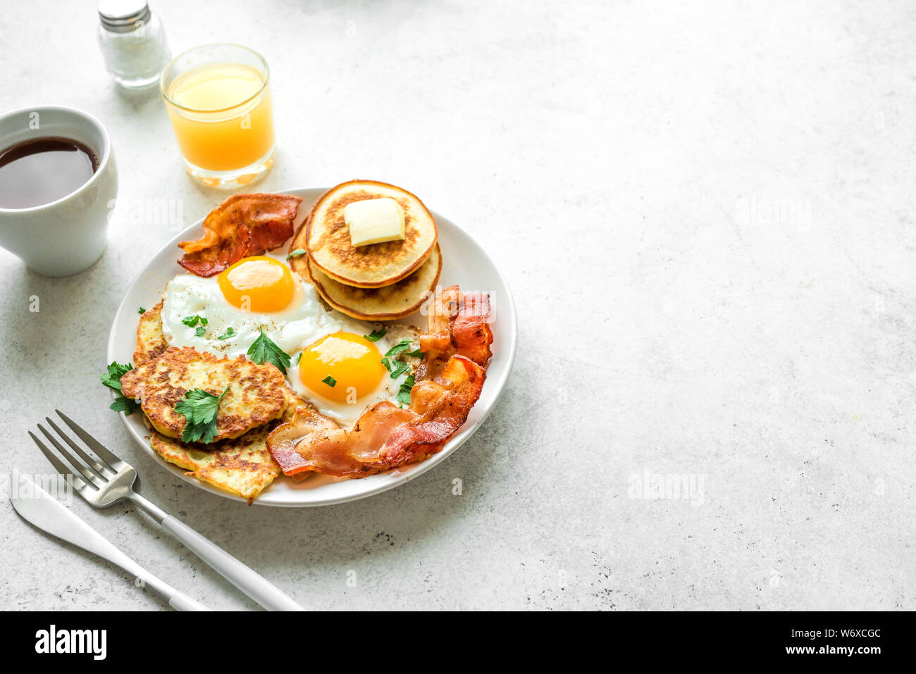 Amerikanisches Frühstück auf weißem Tabelle, aus der Nähe. Sonnenseite gebratene Eier, gebratenen Speck, Hash Brown, Pfannkuchen, Orangensaft und Kaffee zum Frühstück. Stockfoto