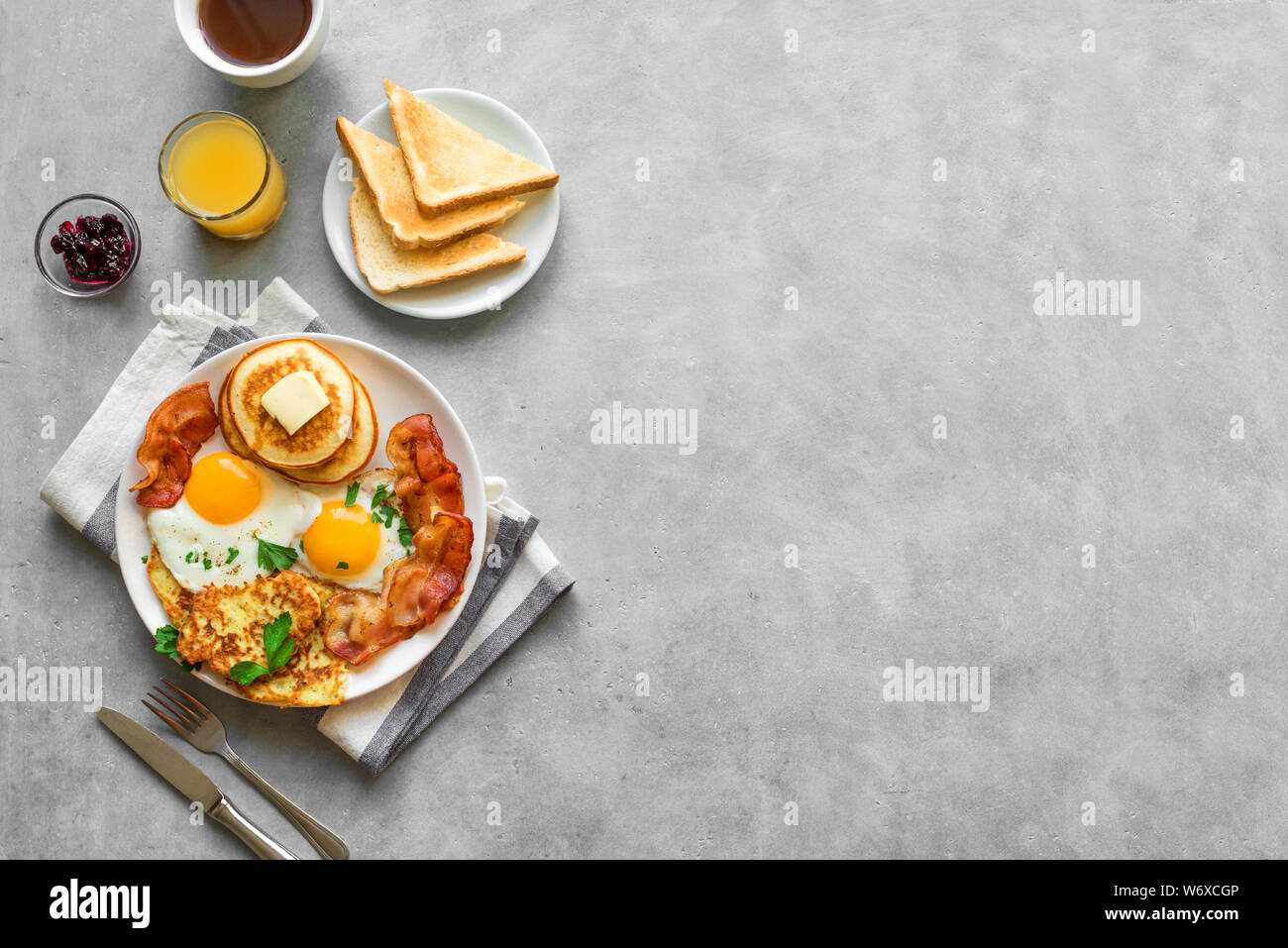 Amerikanisches Frühstück auf grau, Ansicht von oben, kopieren. Sonnenseite gebratene Eier, gebratenen Speck, Hash Brown, Pfannkuchen, Toast, Orangensaft und Kaffee für Stockfoto