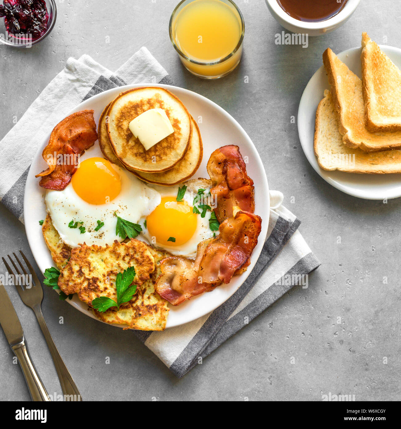 Amerikanisches Frühstück auf grau Tabelle, aus der Nähe. Sonnenseite gebratene Eier, gebratenen Speck, Hash Brown, Pfannkuchen, Orangensaft und Kaffee zum Frühstück. Stockfoto