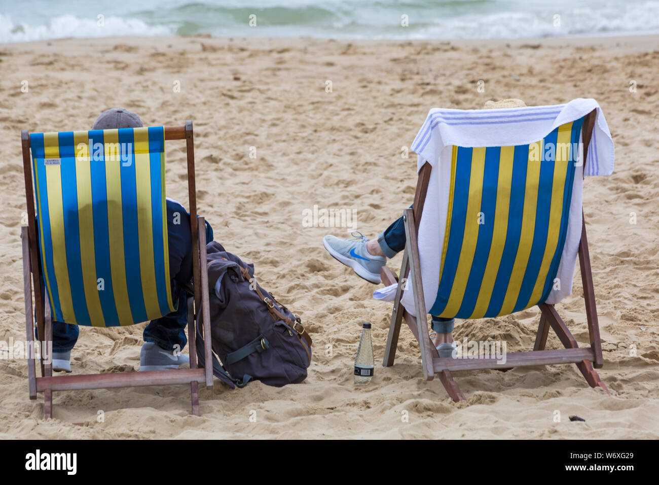 Bournemouth, Dorset UK. August 2019. Wetter in Großbritannien: Bedeckt und bewölkt, aber warm und nebelig. Strandbesucher gehen zu den Stränden von Bournemouth, um das warme Wetter zu genießen. Ein Paar erholt sich in Liegestuhlen am Strand - Rückansicht, Rückansicht. Credit: Carolyn Jenkins/Alamy Live News Stockfoto