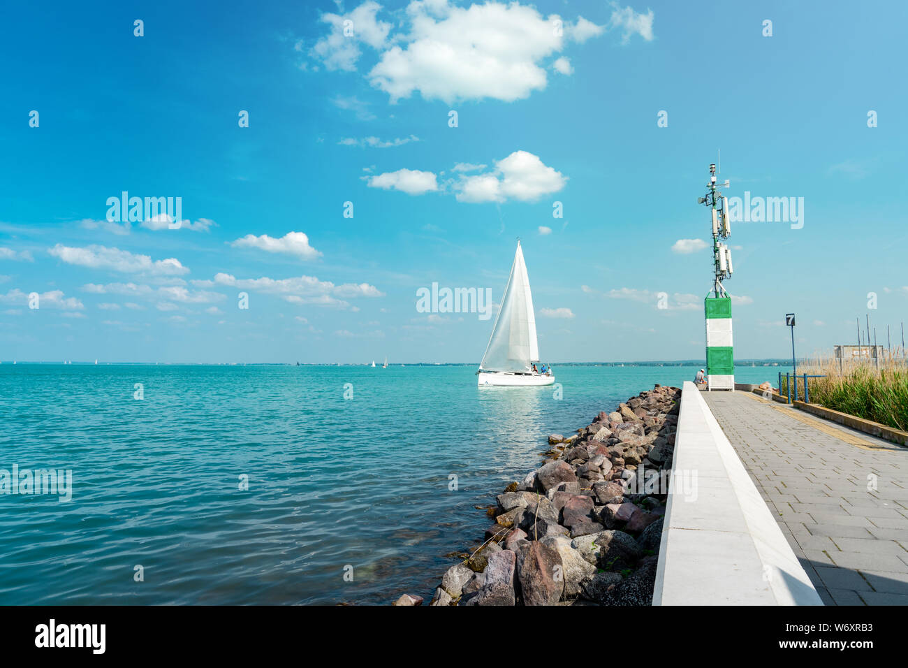 Segelboot auf dem Blue Lake Balaton in Ungarn mit Pier und Felsen an der Küste lkeside Stockfoto