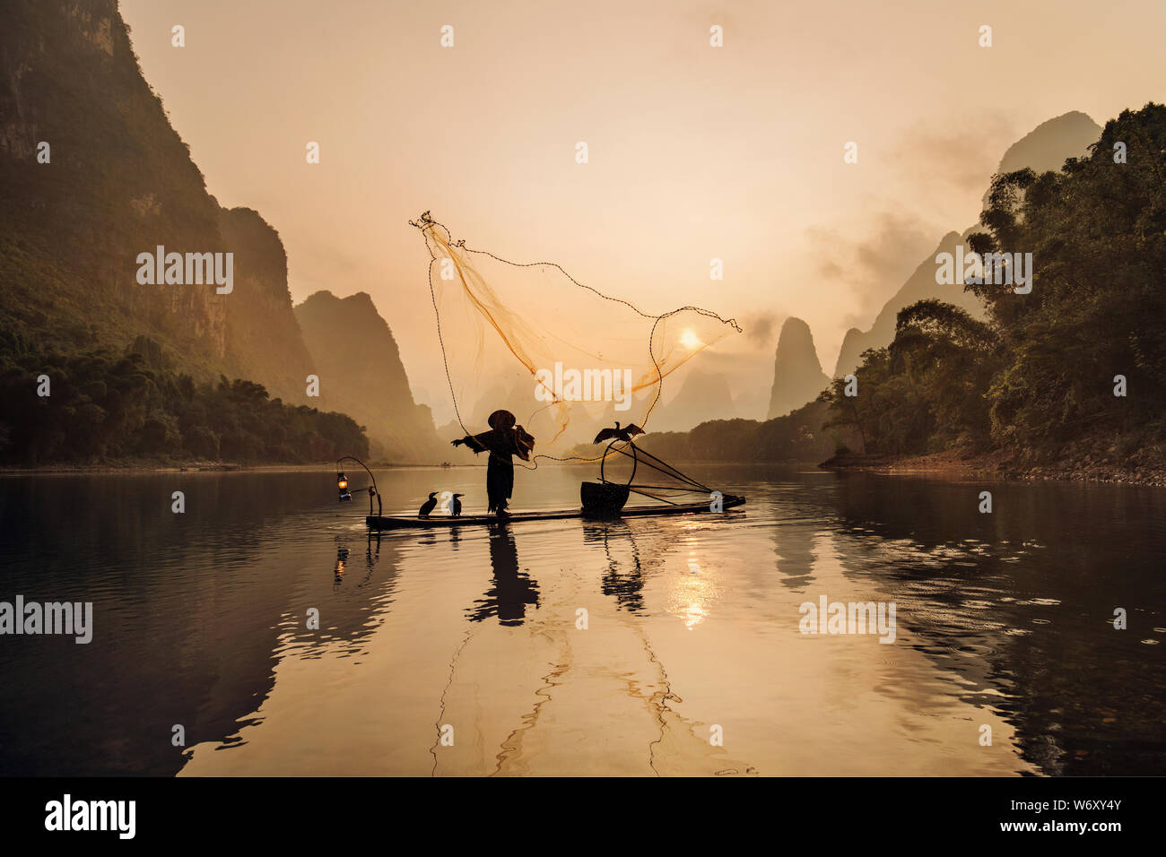 Traditionelle Kormoran Fischer, Blackbeard casting einem Fischernetz bei Sonnenaufgang, in der Nähe von Xingping, China. Stockfoto