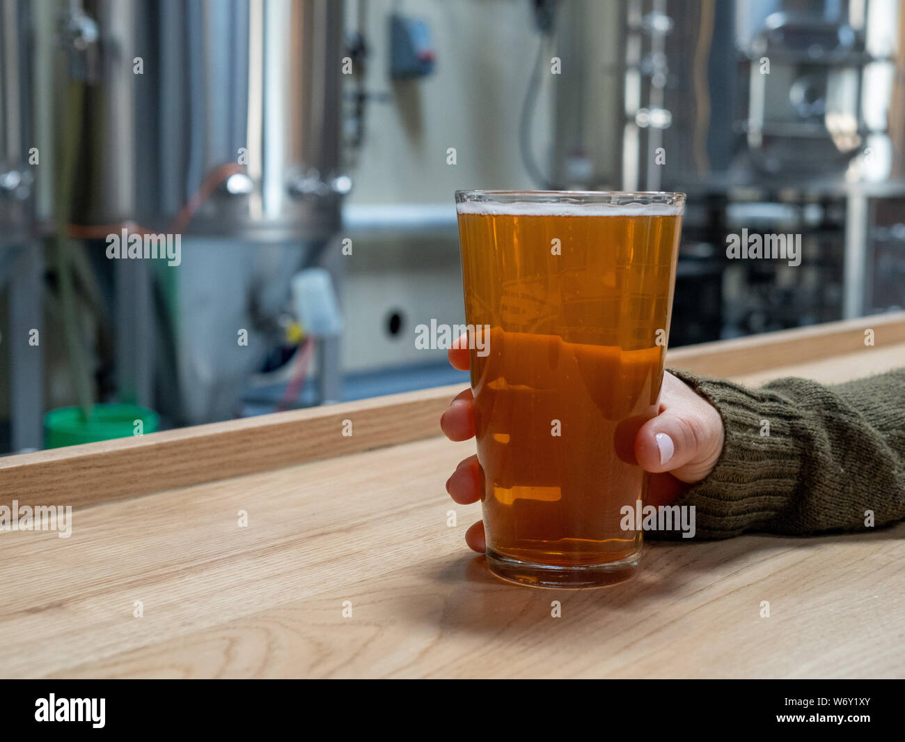 Frauen, die sich in Pint Bier auf Zähler an der Vorderseite des Gärtanks und Brauereianlagen Stockfoto