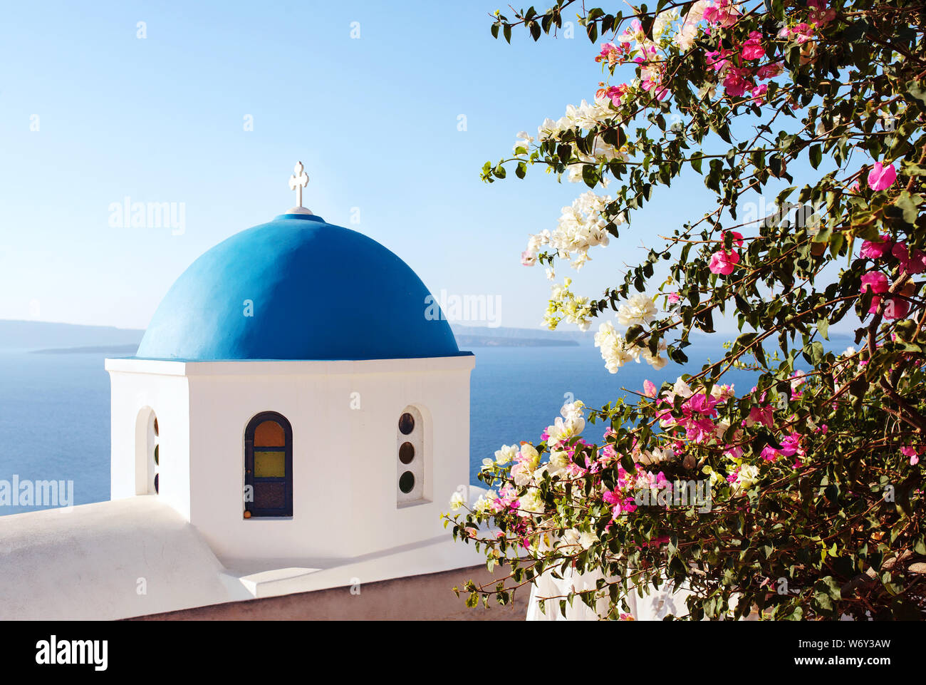 Santorini, eine klassische Ansicht der blauen Kuppel Kirche mit bugambilia Blumen. Das Dorf Oia, Griechenland. Stockfoto