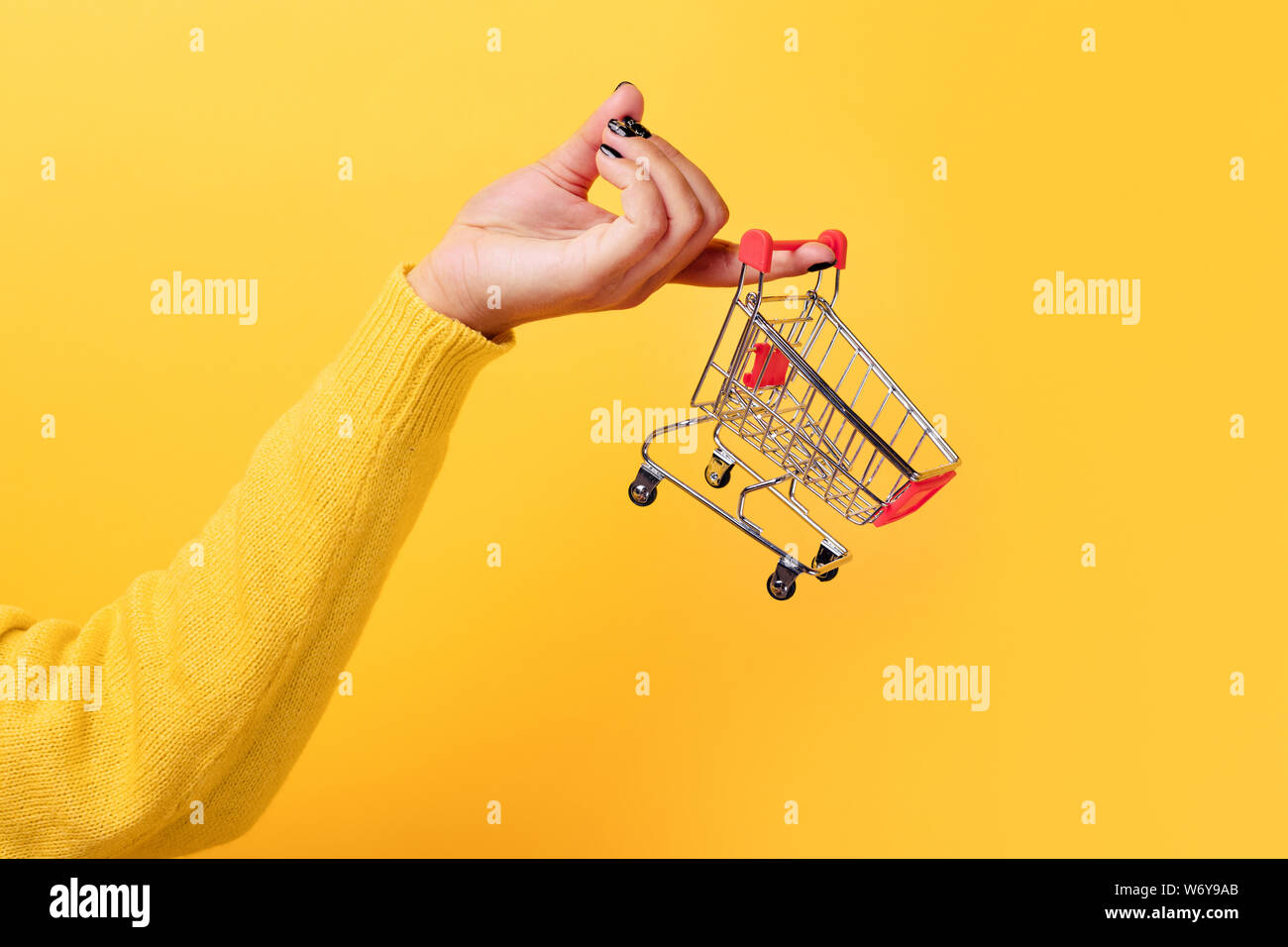 Einkaufen am Markt Geschäfte Konzept. Frau Hand kleine winzige Warenkorb Trolley über Trend auf gelbem Hintergrund Stockfoto