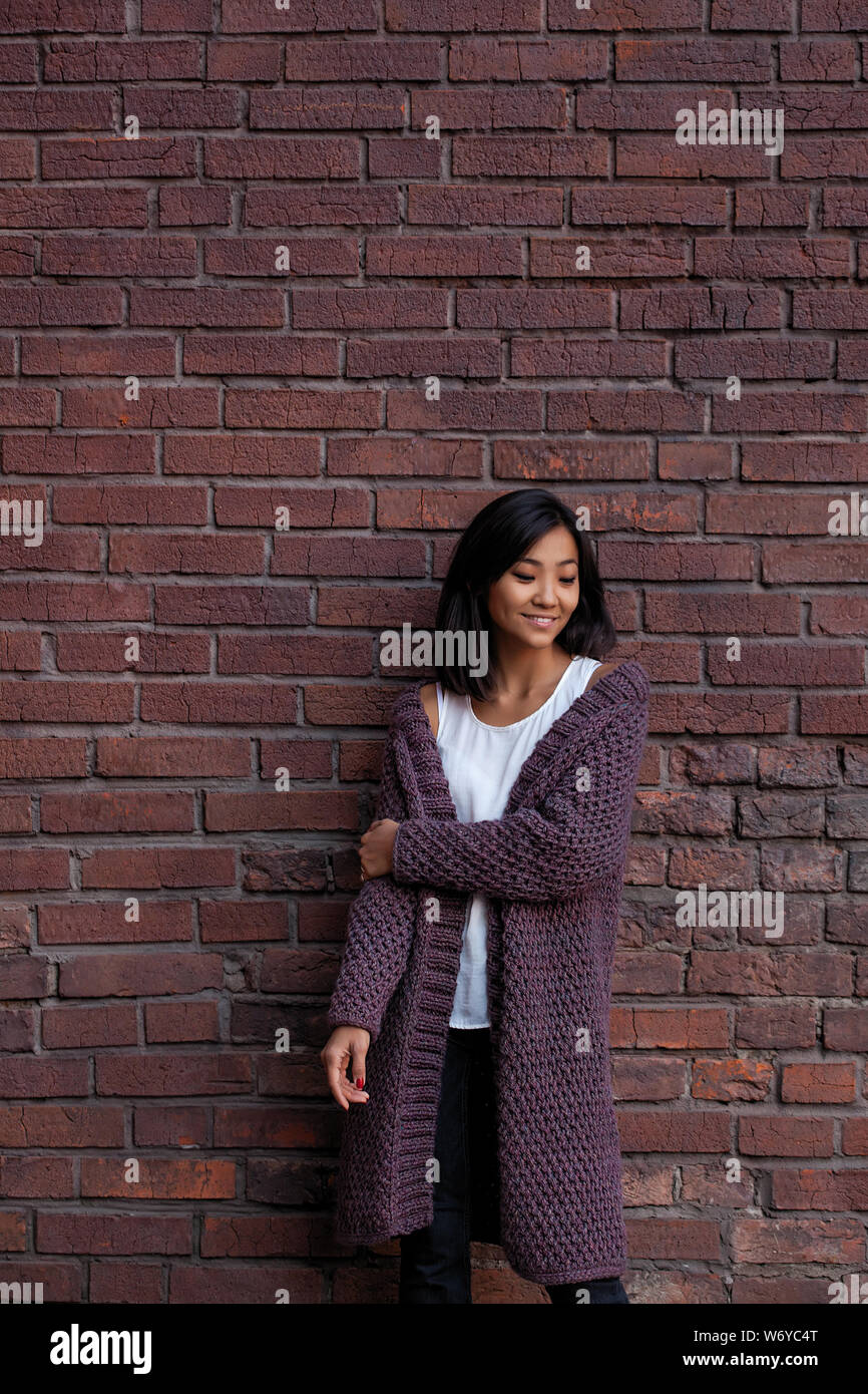 Lächelnd glücklich asiatischen Mädchen in warmen Violett Cardigan in der Nähe von Mauer Stockfoto