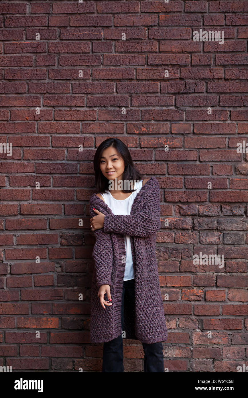 Lächelnd glücklich asiatischen Mädchen in warmen Violett Cardigan in der Nähe von Mauer Stockfoto