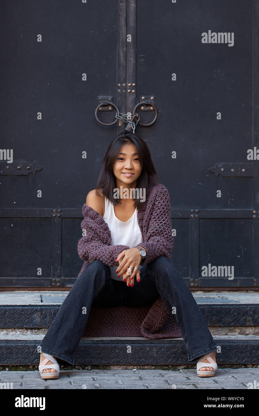 Schöne asiatische Mädchen in einem violetten Strickjacke sitzt auf der Treppe in der Nähe von zu Haus Stockfoto