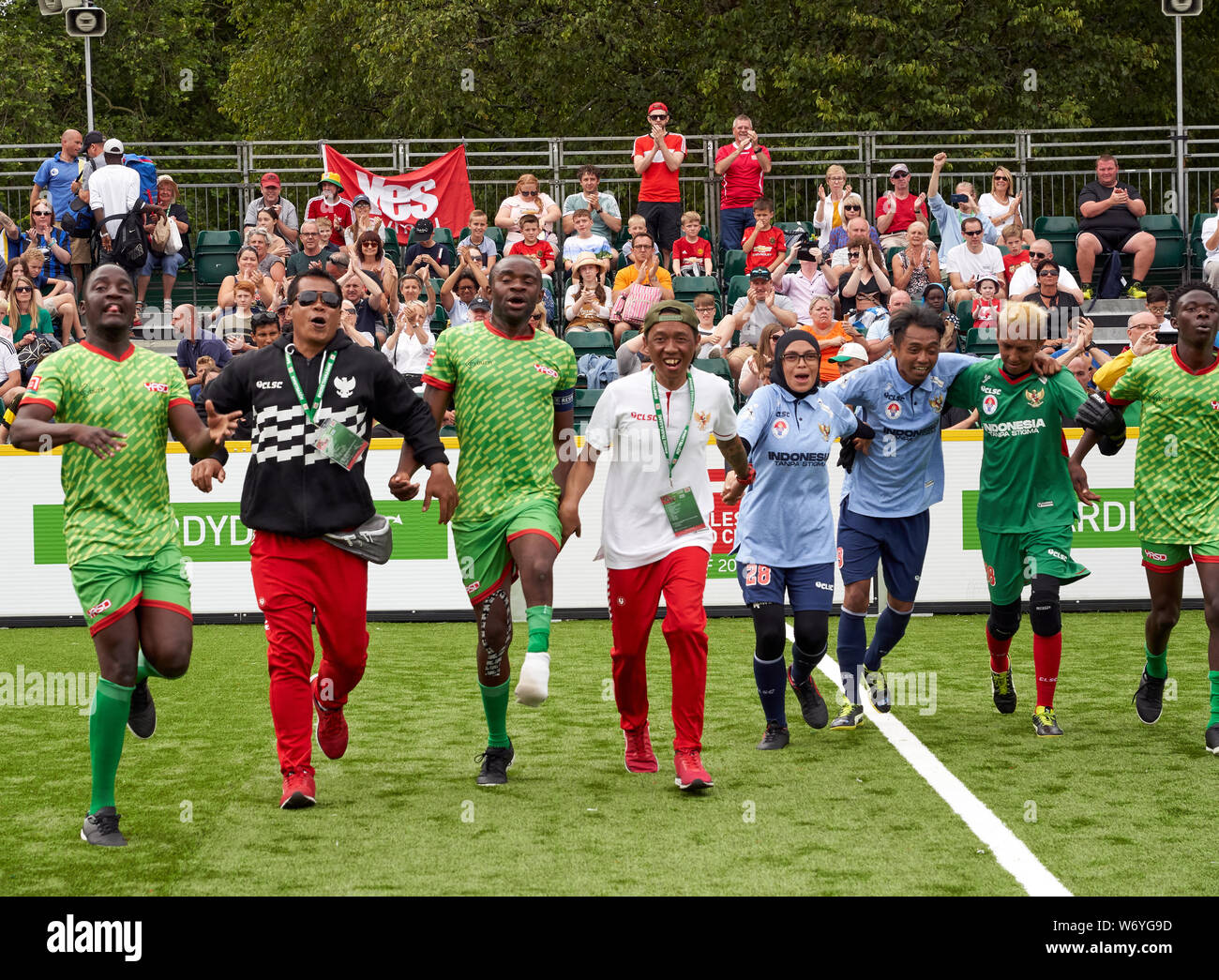 Spieler in der Indonesien und Simbabwe Fußball-Teams feiern am Ende ihres Gleichen an den Homeless World Cup, Cardiff 2019 Stockfoto