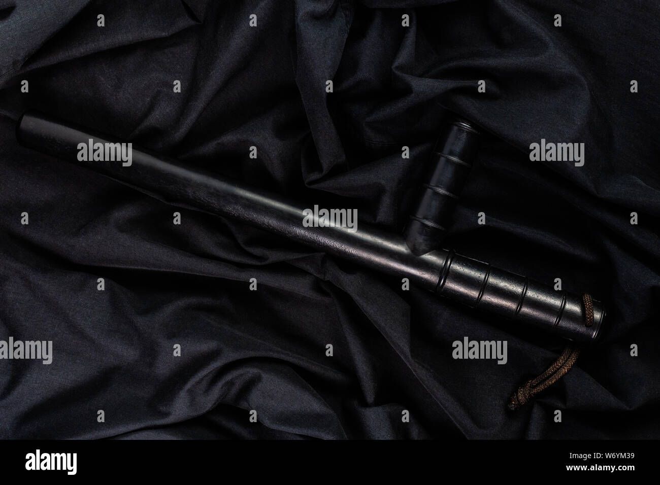 Gummi schwarz Polizei Schlagstock auf schwarzem Shirt zerknittert Tuch low-key-Flach. Stockfoto