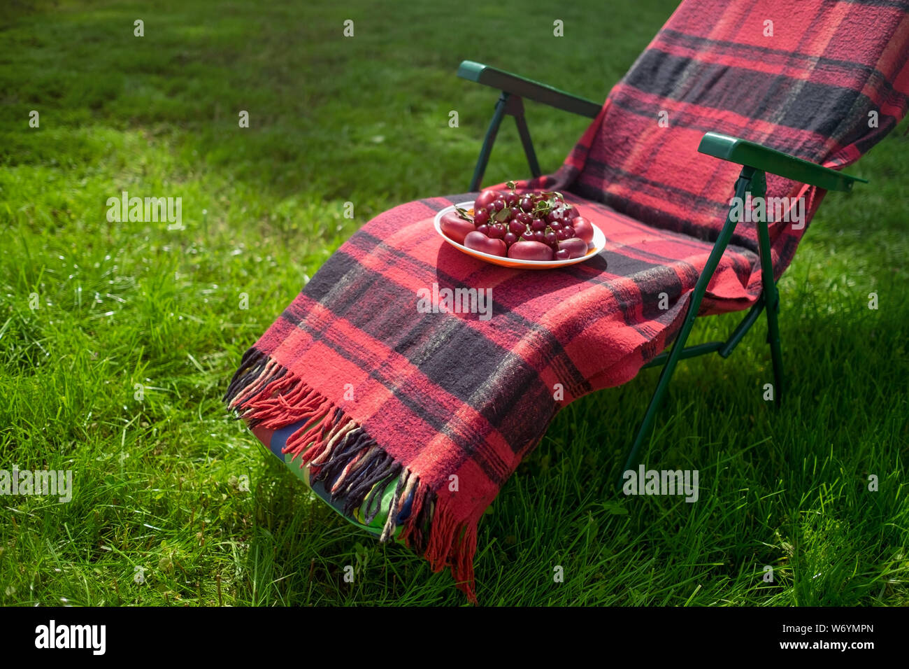 Mit Kirschen auf einem Stuhl in einem grünen Garten Platte Stockfoto