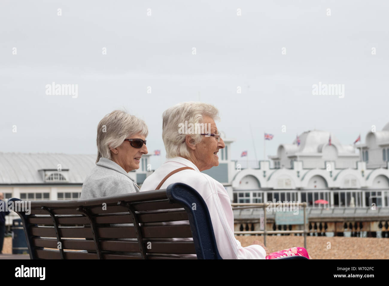 Zwei ältere Damen oder Frauen saßen auf einer Bank im Gespräch an der englischen Küste Stockfoto