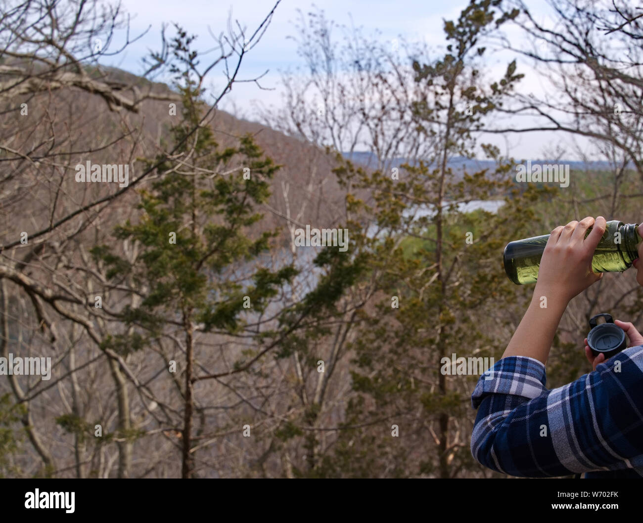 Ein müder Wanderer noch nicht vollendet das Trinken aus einer Flasche Wasser und genießen Sie die Sehenswürdigkeiten auf einem Berg. Stockfoto