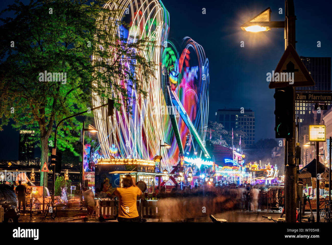 03.August 2019 Hessen, Frankfurt/Main: Während der MAINFEST, einem Karussell hinterlässt seine Spuren von Licht über der Strom der Besucher vorbei. Nach Angaben der Stadt, die Folk Festival, das erste im Jahr 1340 gefeiert wurde zu weihen, in der Nähe der Dreikönigskirche (Kirche der Heiligen Drei Könige), war ursprünglich eine Rettungsleine, die von Fischern und Seglern an den Main. Es findet vom 2. August bis zum 5. August 2019. Foto: Frank Rumpenhorst/dpa Stockfoto