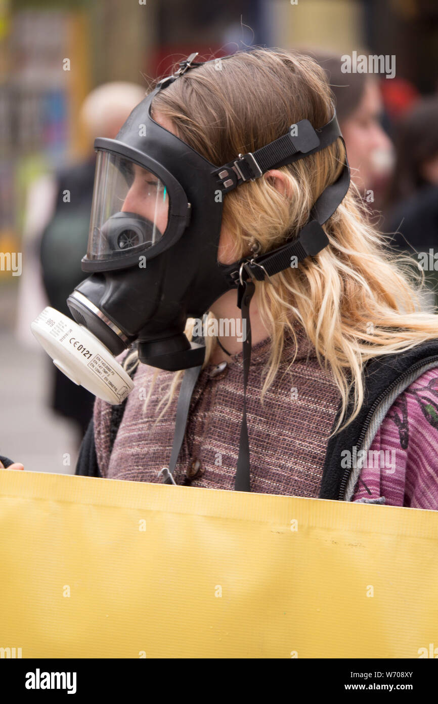 Junge, blonde Frau trägt einen schwarzen Gasmaske Holding eine helle gelbe Klima Not banner Unterbrechung des Verkehrs in der Innenstadt von Melbourne, Australien. Stockfoto