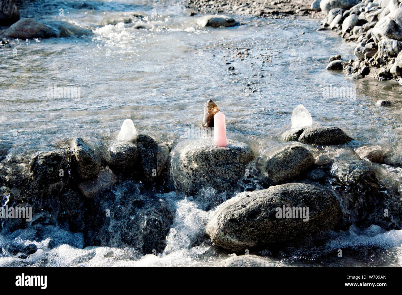 Rose Quartz Crystal und andere Kristalle auf einem Stein im Fluss gereinigt wird Energie durch das Sonnenlicht und das fließende Wasser. Still Life Fotografie. Stockfoto