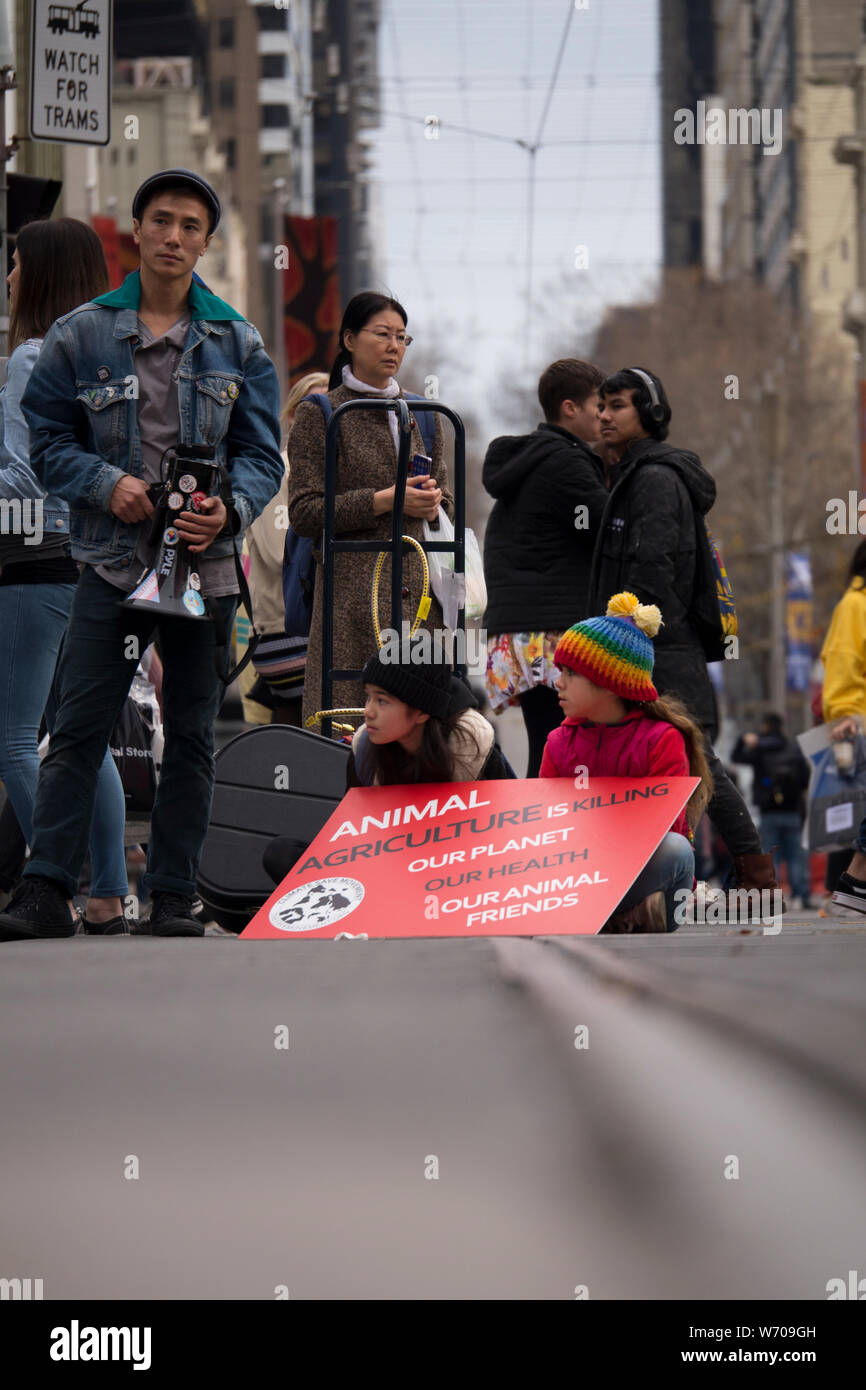 Zwei kleine Kinder sitzen auf Straßenbahnschienen mit roten Klima Not sign an Demonstration in der Innenstadt von Melbourne, Australien Klima protestieren. Stockfoto