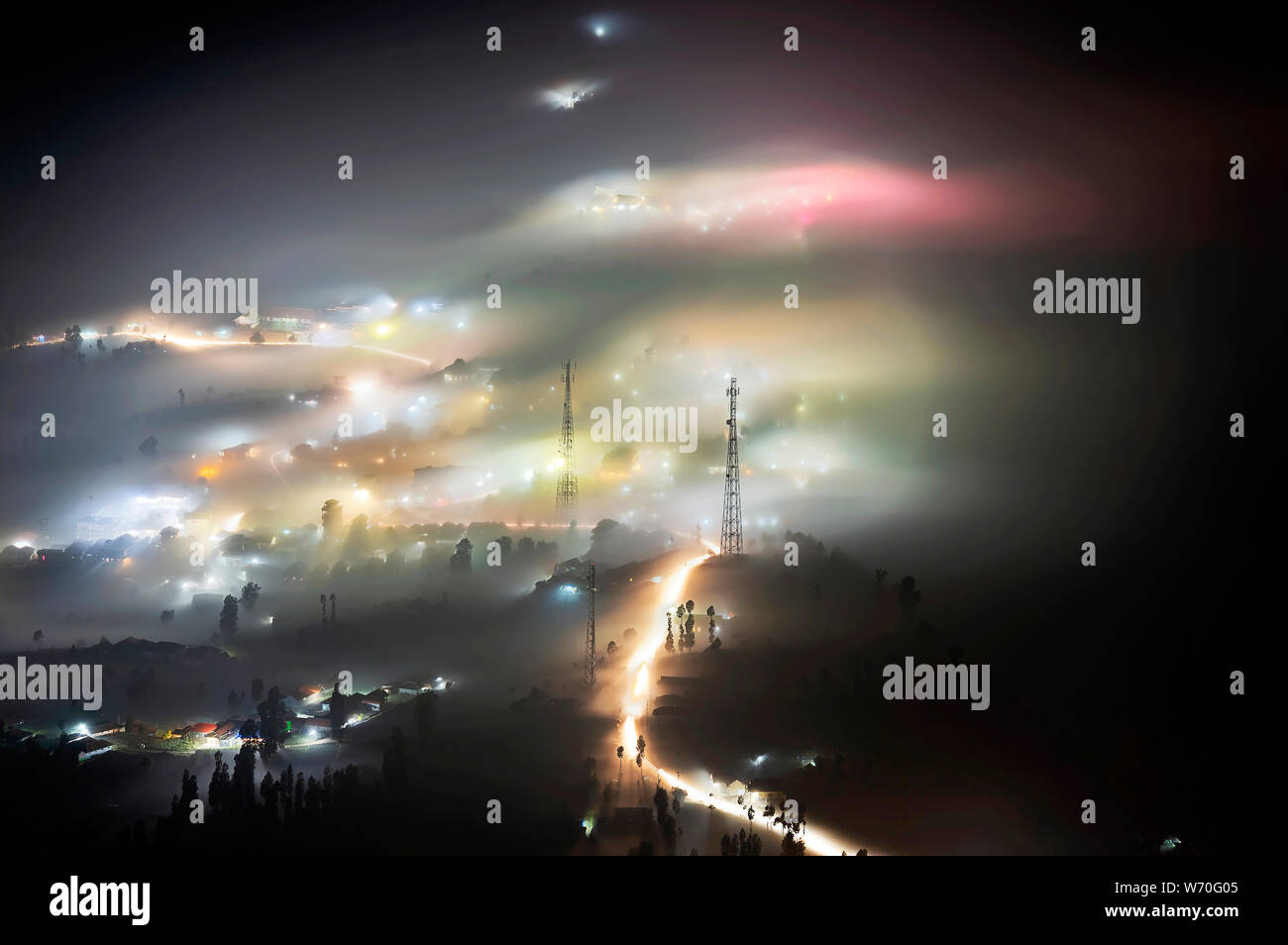 Nebel, der sich in einem kleinen Dorf und Bäume in der Nähe von Mount Bromo bei Nacht Stockfoto