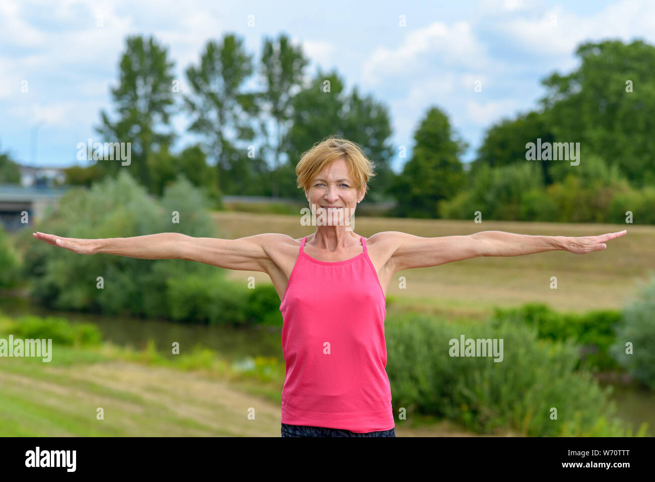 Fit gesund schlank Frau mittleren Alters heraus halten Sie die Arme an der Seite in einem farbenfrohen rosa Sport top draußen in der Landschaft Stockfoto