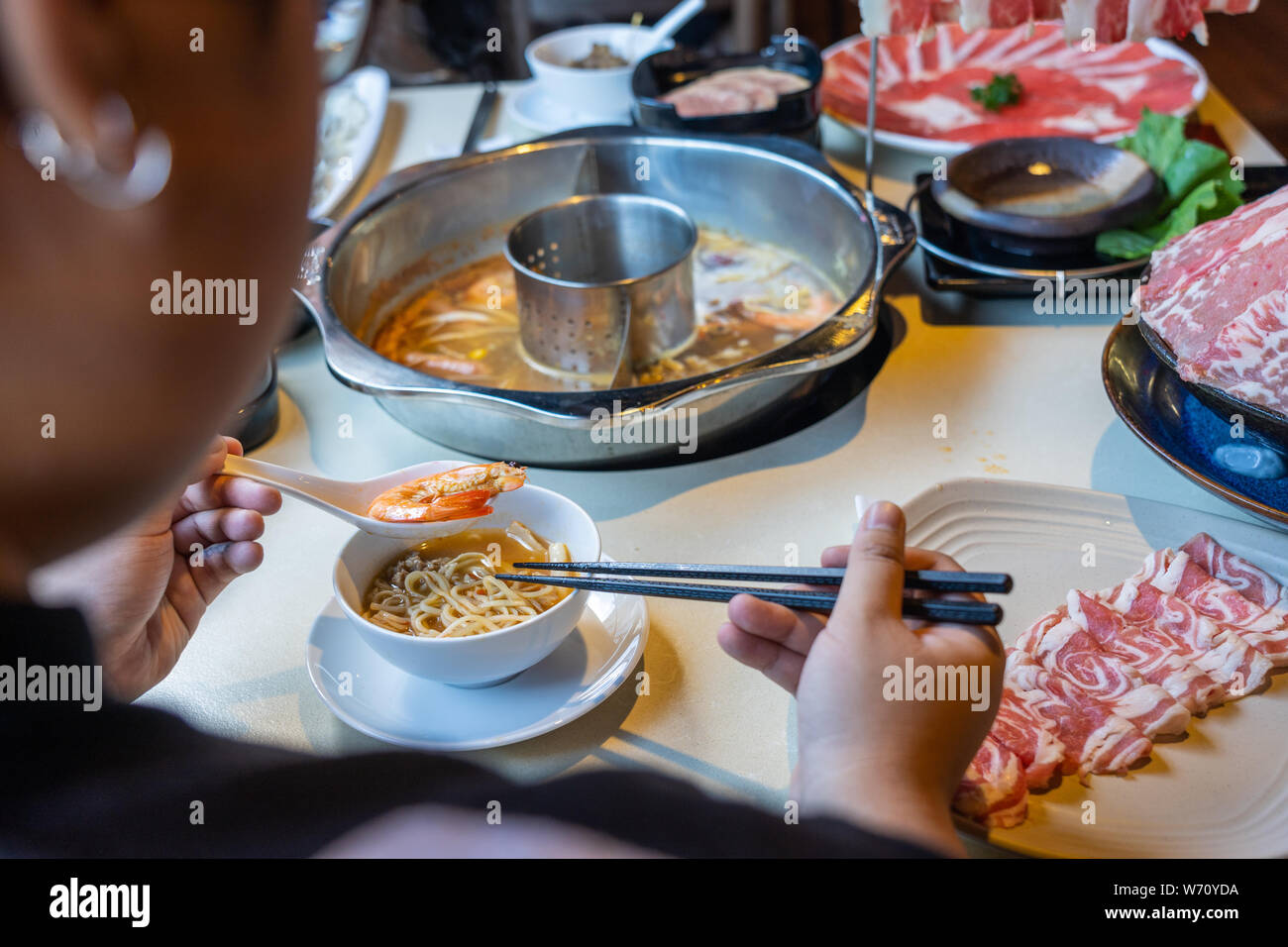 Frau mit Essstäbchen und Löffel essen im asiatischen Stil Seafood hotpot Stockfoto