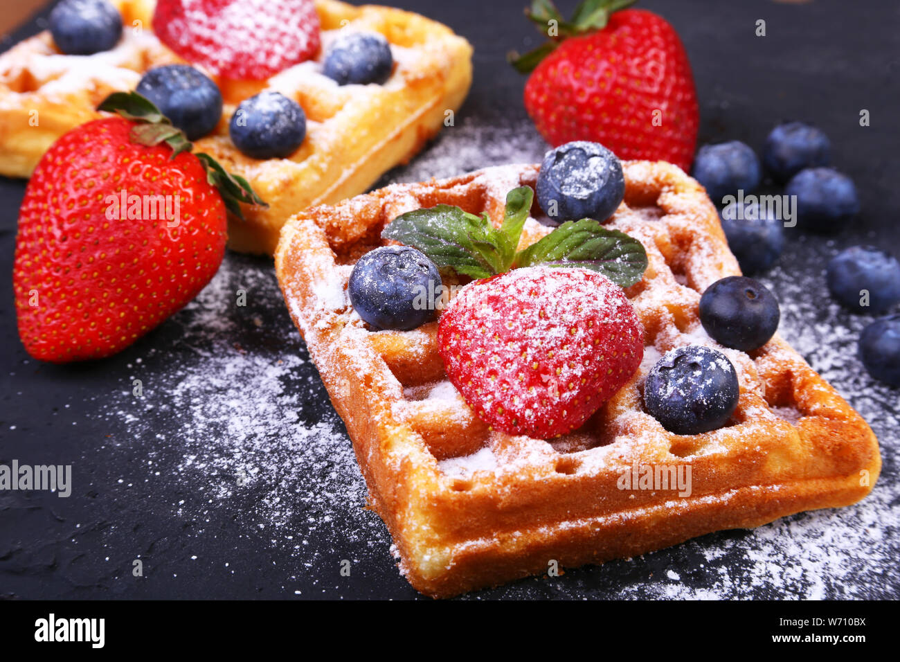 Hausgemachte, traditionelle belgische Waffeln mit frischen Obst, Beeren und Zucker Puder auf schwarze Platte Stockfoto