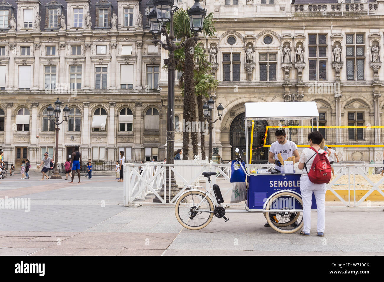 Paris Street Food - eine Frau Tourist kauft ein Eis Senoble von einem Fahrrad Warenkorb auf einer Straße in Paris. Frankreich, Europa. Stockfoto