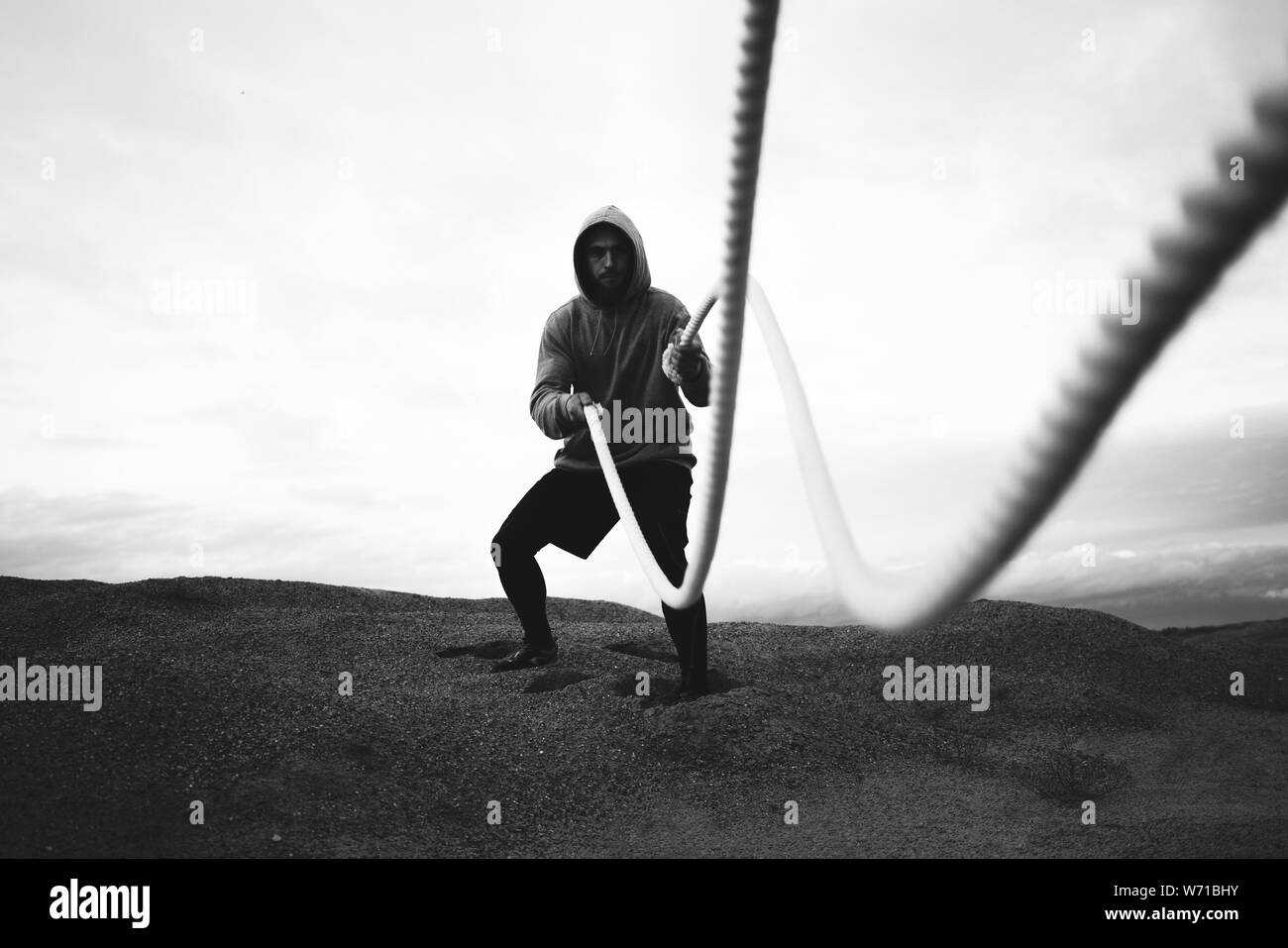 Mutige Athleten mit Sportswear, intens Trainings mit Schlacht Seile auf Outdoor. Fitness mutiger Mann tun Fitness Workout am Strand. Schwarz und Weiß Stockfoto