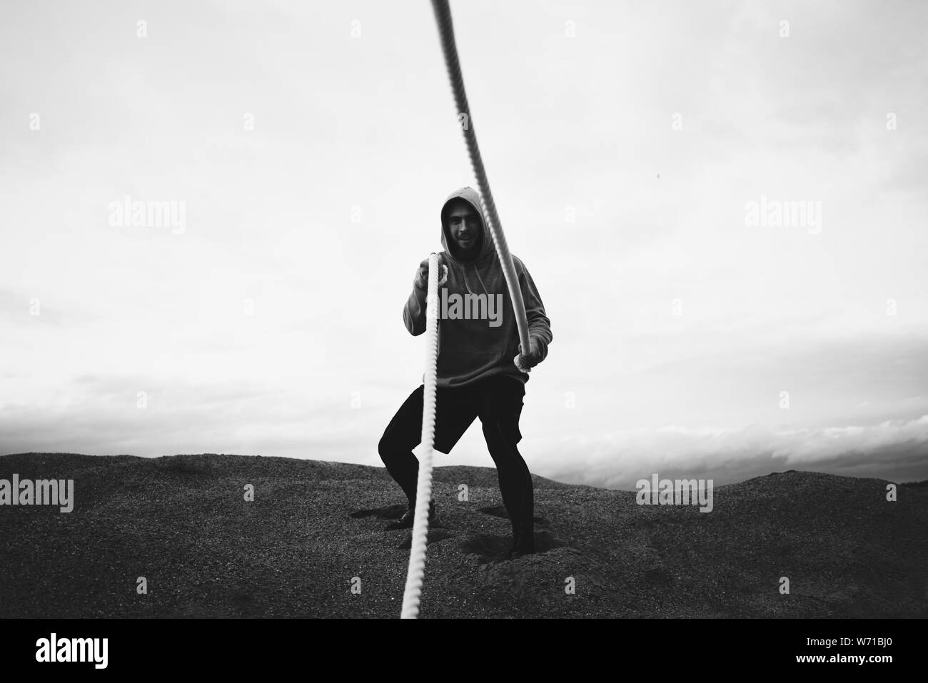 Starke Mann, Sportbekleidung, Fitness Workout am Strand. Fitness mutiger Mann tun intens Workout mit Schlacht Seile auf Outdoor. Schwarze und weiße Col Stockfoto