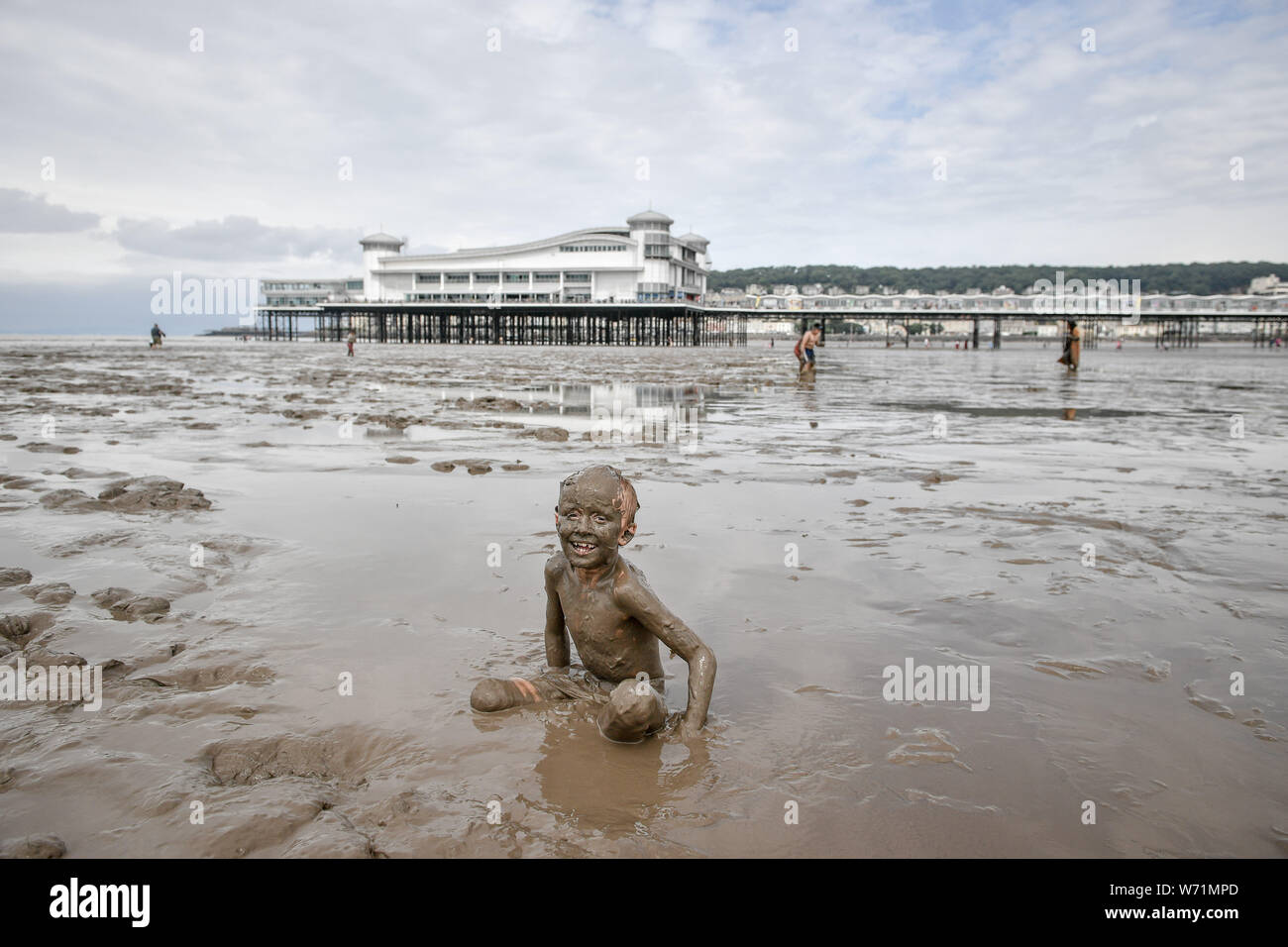 Blaze, 8, von Swindon, ist von Kopf bis Fuß bedeckt, wie er in den Schlamm in Weston-super-Mare Beach als der Gezeiten liegender und die riesige Ausdehnung des Wattenmeer spielt den Strand Abdeckung wo Urlauber Plantschen genießen. Stockfoto