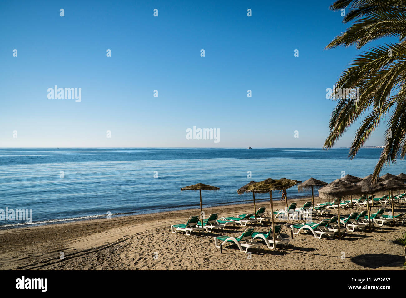 Blick auf den Strand von Marbella, Spanien. Mit leeren Liegestühlen, Stroh Schirme, Mittelmeer und strahlend blauer Himmel Stockfoto