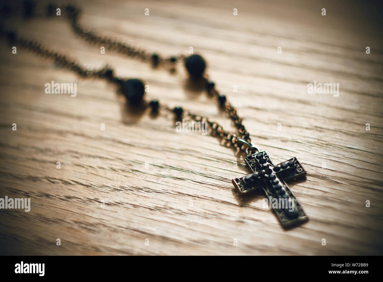 Metal Gothic Black Cross mit schwarzen Perlen auf der Kette liegt auf dem alten Holz- Oberfläche, durch Licht beleuchtet. Stockfoto