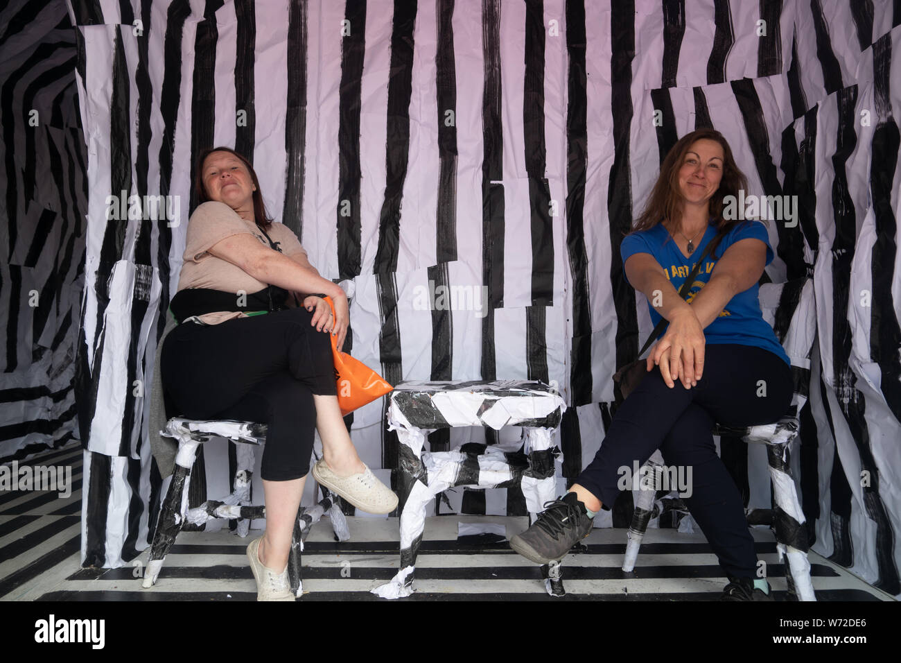 Zwei Frauen sitzen auf Stühlen im interaktiven Karima Klasen's Kunst Installation bestehend aus schwarz-weiß gestreiften gewickelt. Orebro, Schweden Stockfoto