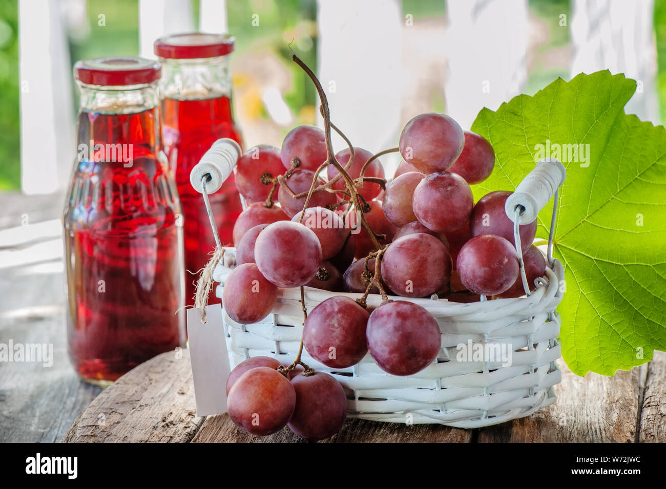 Ein Bündel rosa Trauben, vorbereitet, um den Saft zu extrahieren, ist in einem weißen Korb . Zwei Flaschen Traubensaft stehen auf dem Tisch neben einem Traubenhaufen Stockfoto