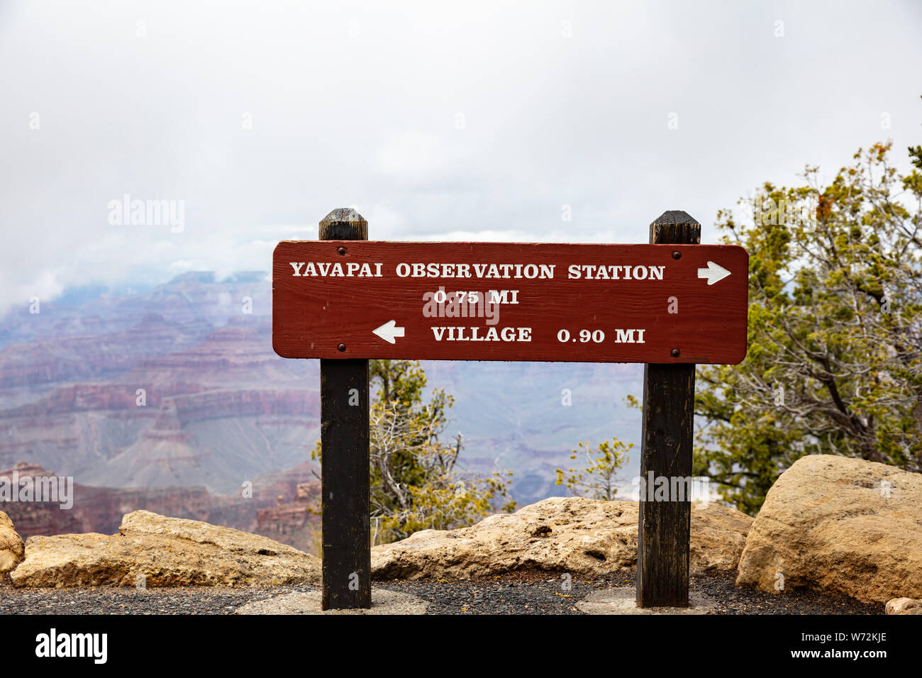Grand Canyon, Arizona, USA. 22. Mai 2019. Holzschild mit Informationen und Wegbeschreibungen, roten Felsen Schlucht und bewölkter Himmel Hintergrund Stockfoto