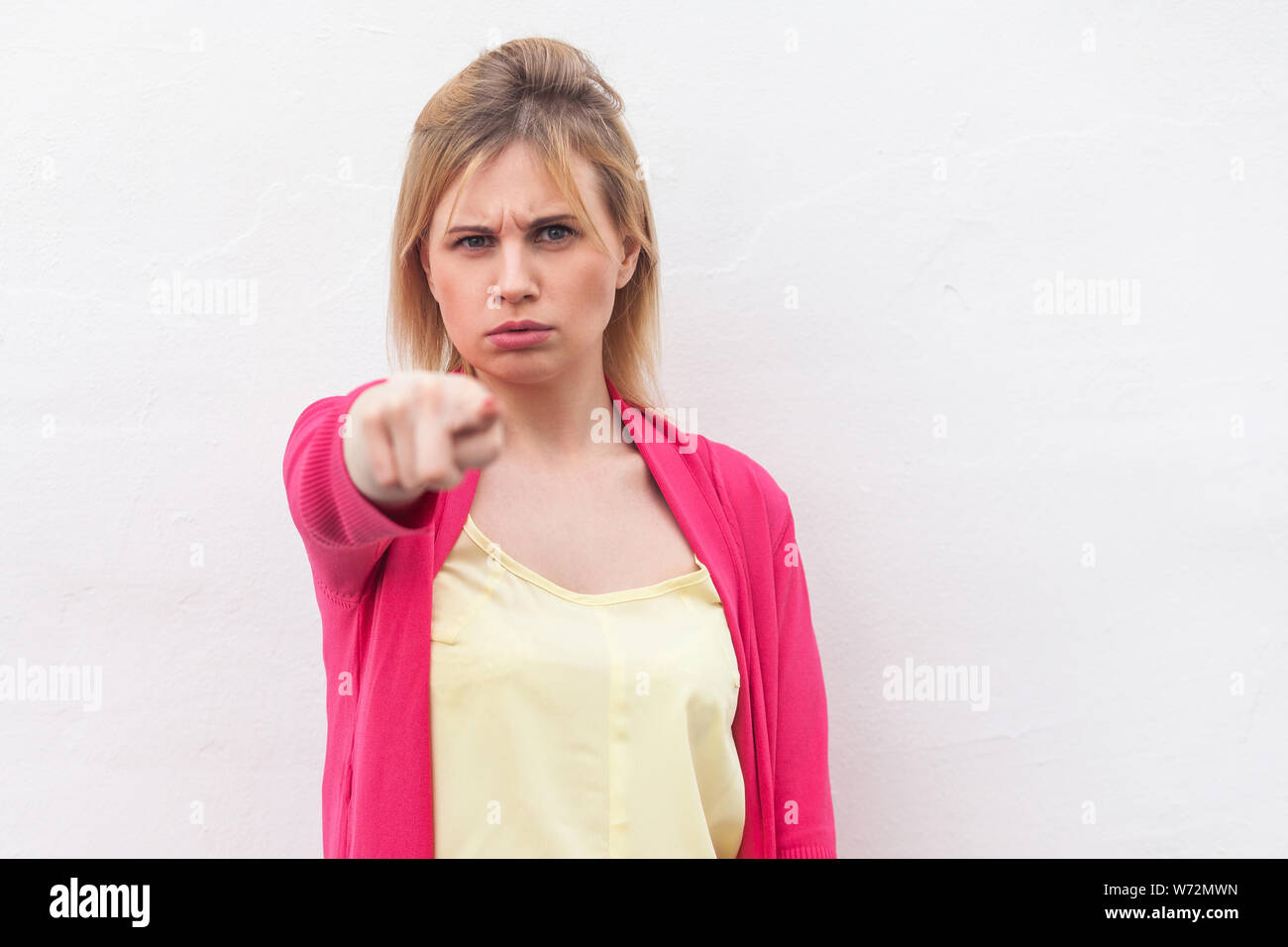 Porträt von Ernst schöne blonde junge Frau im gelben Hemd und roter Bluse stehen, schauen und zeigen auf Kamera mit schweren wütend das Gesicht Pflege. Stockfoto