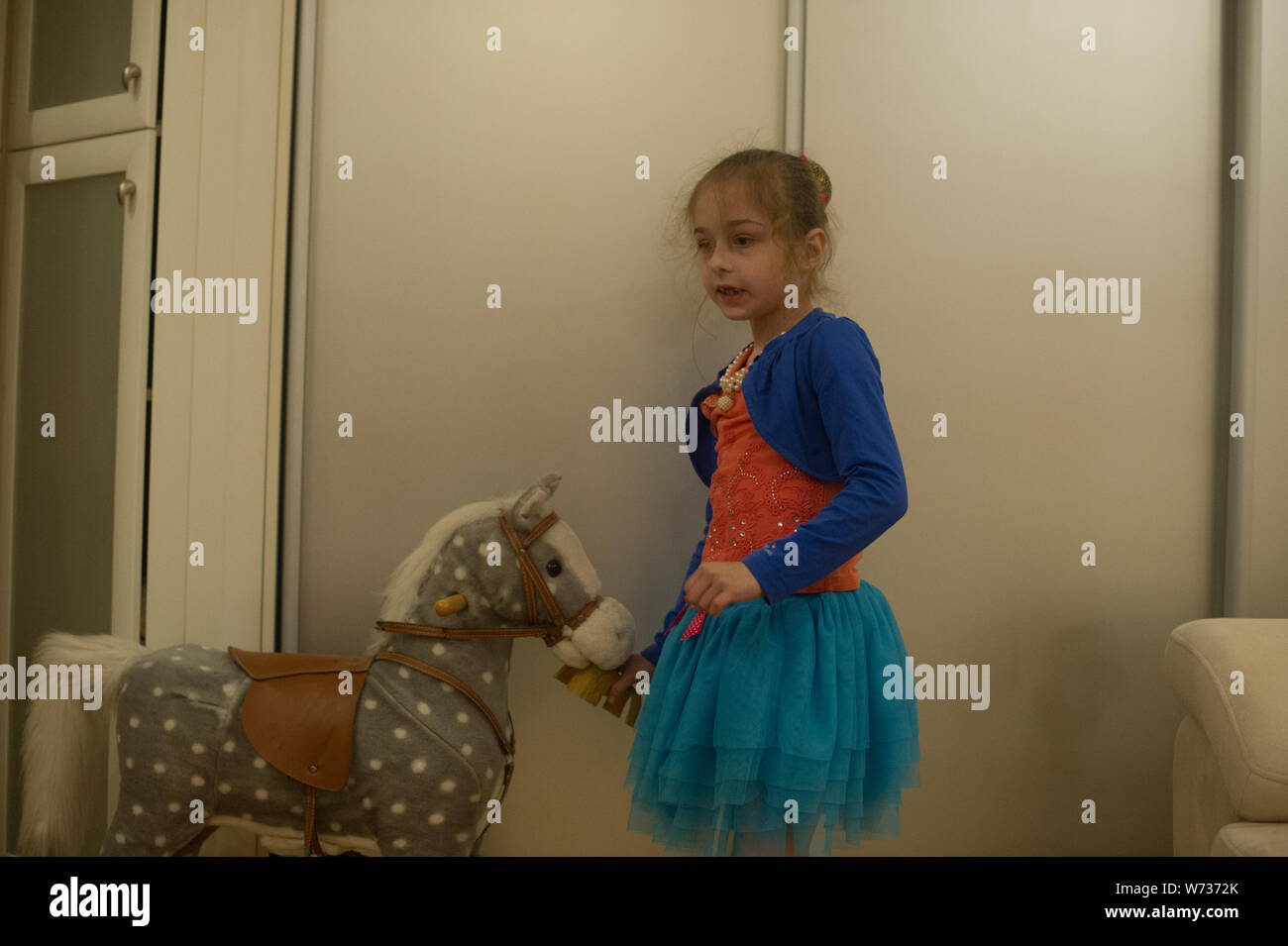 Kleines Mädchen spielt mit einem Pferd Gurney. Das Kind sitzt auf einem Pferd. Schöne Mädchen ist glücklich sitzen auf einem Spielzeug Pferd. Einen blauen Rock, eine orange Stockfoto